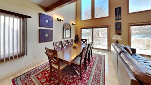 Un comedor con una mesa y sillas de madera, un tapete rojo estampado y ventanas amplias con vistas al exterior.