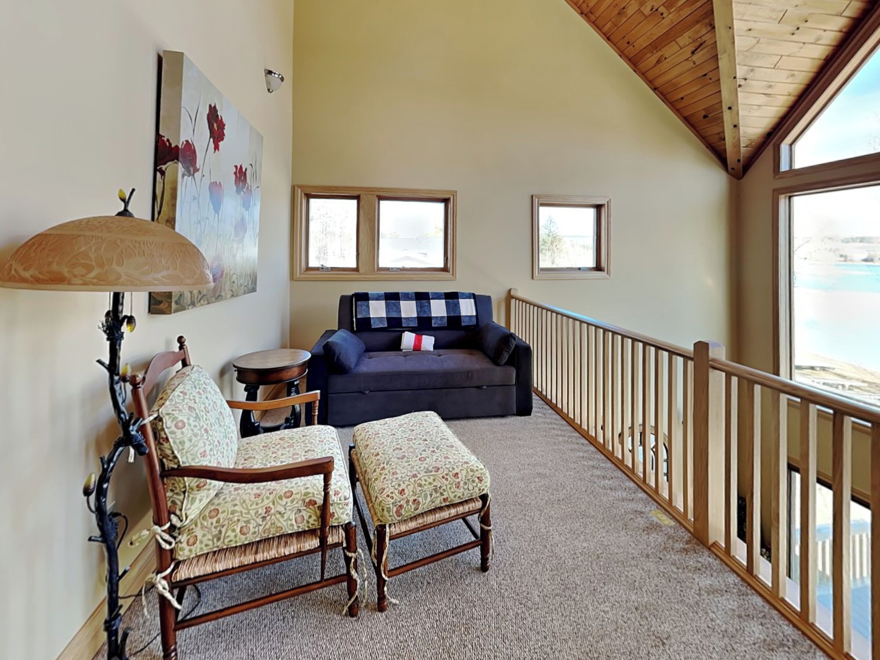 A cozy living room with a wooden ceiling, a sofa, two armchairs, a table, and a view of the sea through large windows.