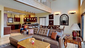 Amplia sala de estar con un gran sofá de cuero marrón, una mesa de centro de madera y una zona de comedor con sillas de madera.