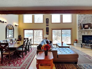 A spacious living room with a large window, a stone fireplace, and a dining area with a red patterned rug. - A Shore Thing by Taylor Made Deep Creek (McHenry)