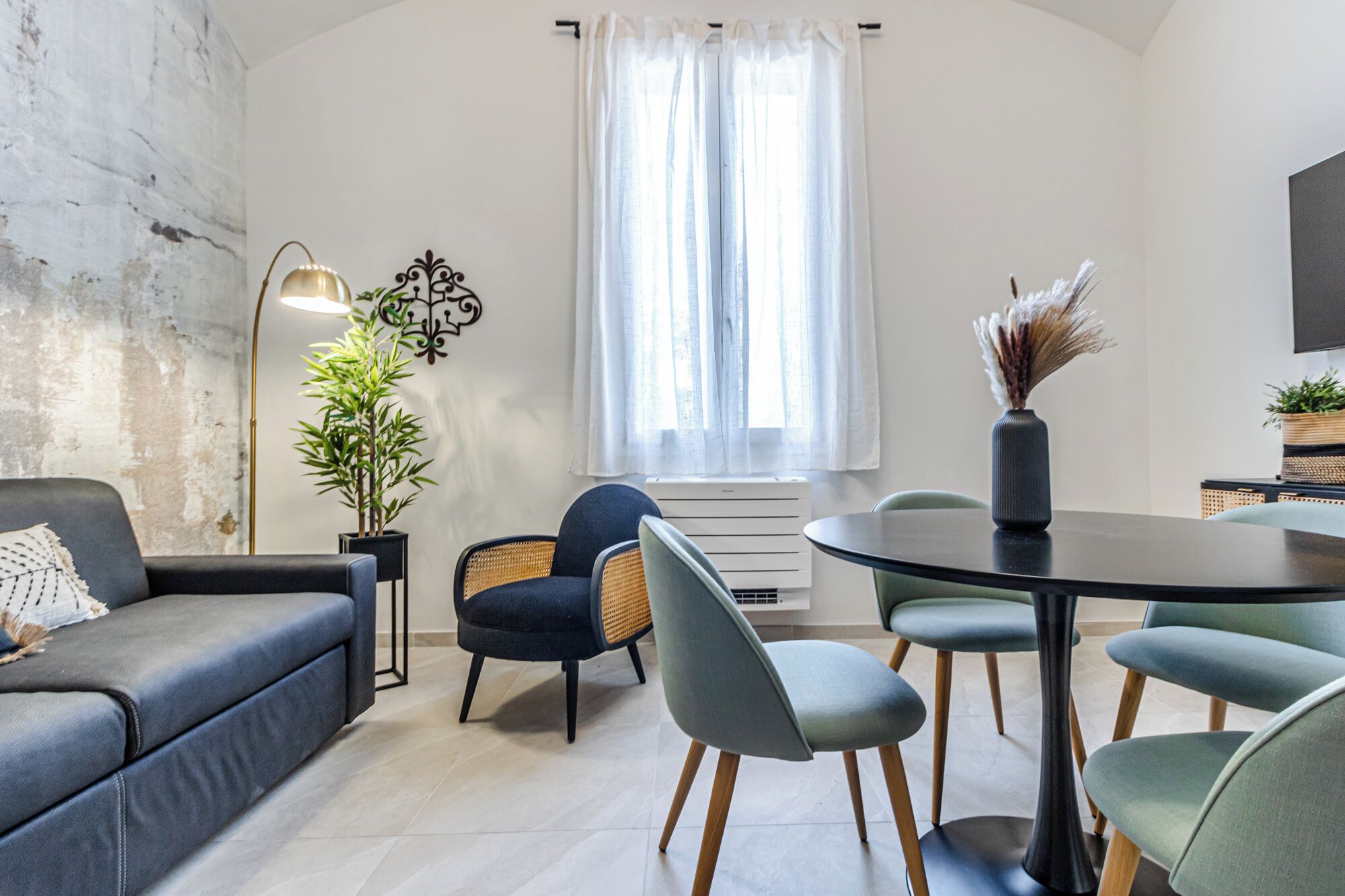 Un salon moderne comprenant un canapé, des fauteuils, une table à manger, une plante en pot et un élément décoratif mural.