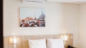 A hotel room with two beds, a wooden headboard, a wall-mounted air conditioner, a nightstand with a phone, and a painting above the beds. - Hotel Triveneto Gramado (Gramado)