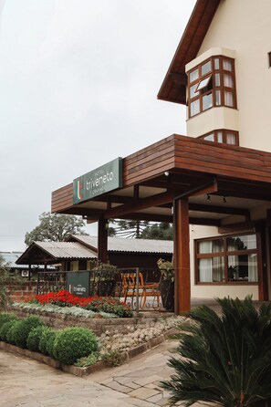 A hotel entrance with a sign, covered outdoor seating, and a landscaped garden. - Hotel Triveneto Gramado (Gramado)