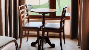 A room with a large window, a wooden table, two chairs, and a bed. - Hotel Triveneto Gramado (Gramado)
