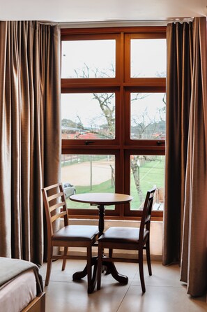 A room with a large window, a wooden table, two chairs, and a bed. - Hotel Triveneto Gramado (Gramado)
