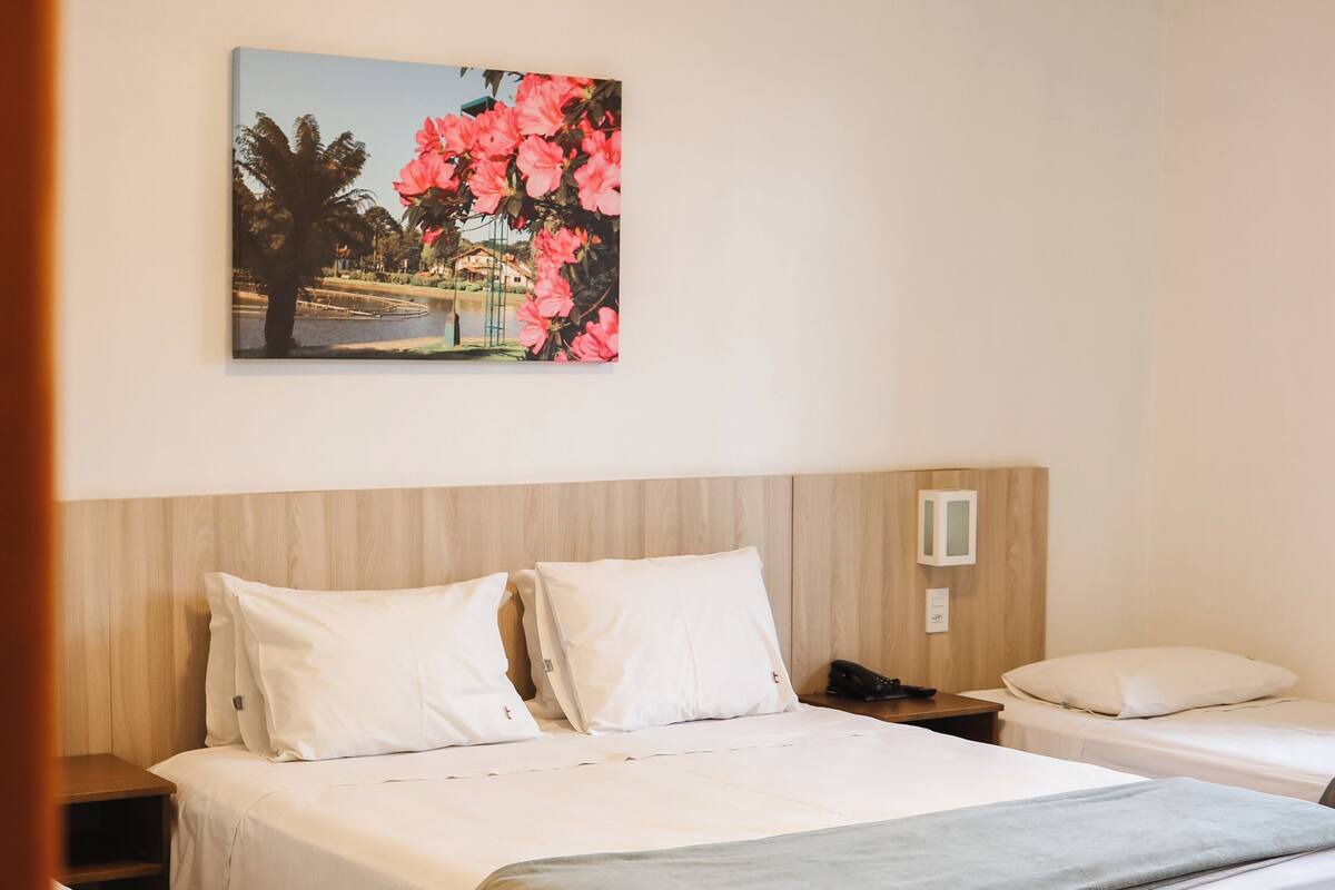 A hotel room with a large bed, a smaller bed, a nightstand, a bedside table, and a painting on the wall.