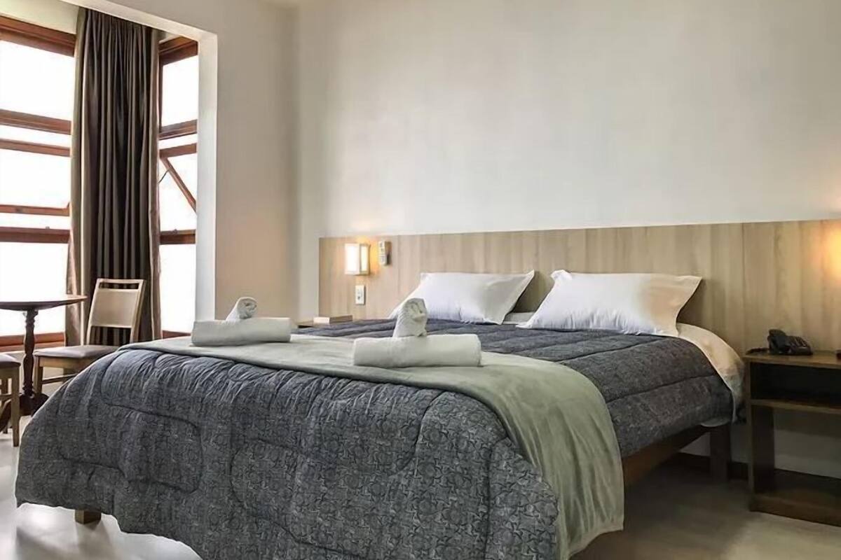 A hotel room with a large bed, a bedside table, a chair, and a window with curtains.