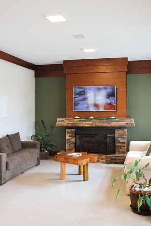 A living room with a fireplace, a sofa, a coffee table, and a television mounted above the fireplace. - Hotel Triveneto Gramado (Gramado)