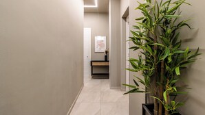 Un pasillo con una gran planta de bambú, un cuadro enmarcado en la pared y un baño moderno con lavamanos y espejo.