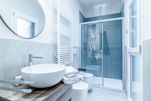 Un bagno moderno con un lavandino bianco di grandi dimensioni, uno specchio, un water e una cabina doccia in vetro.