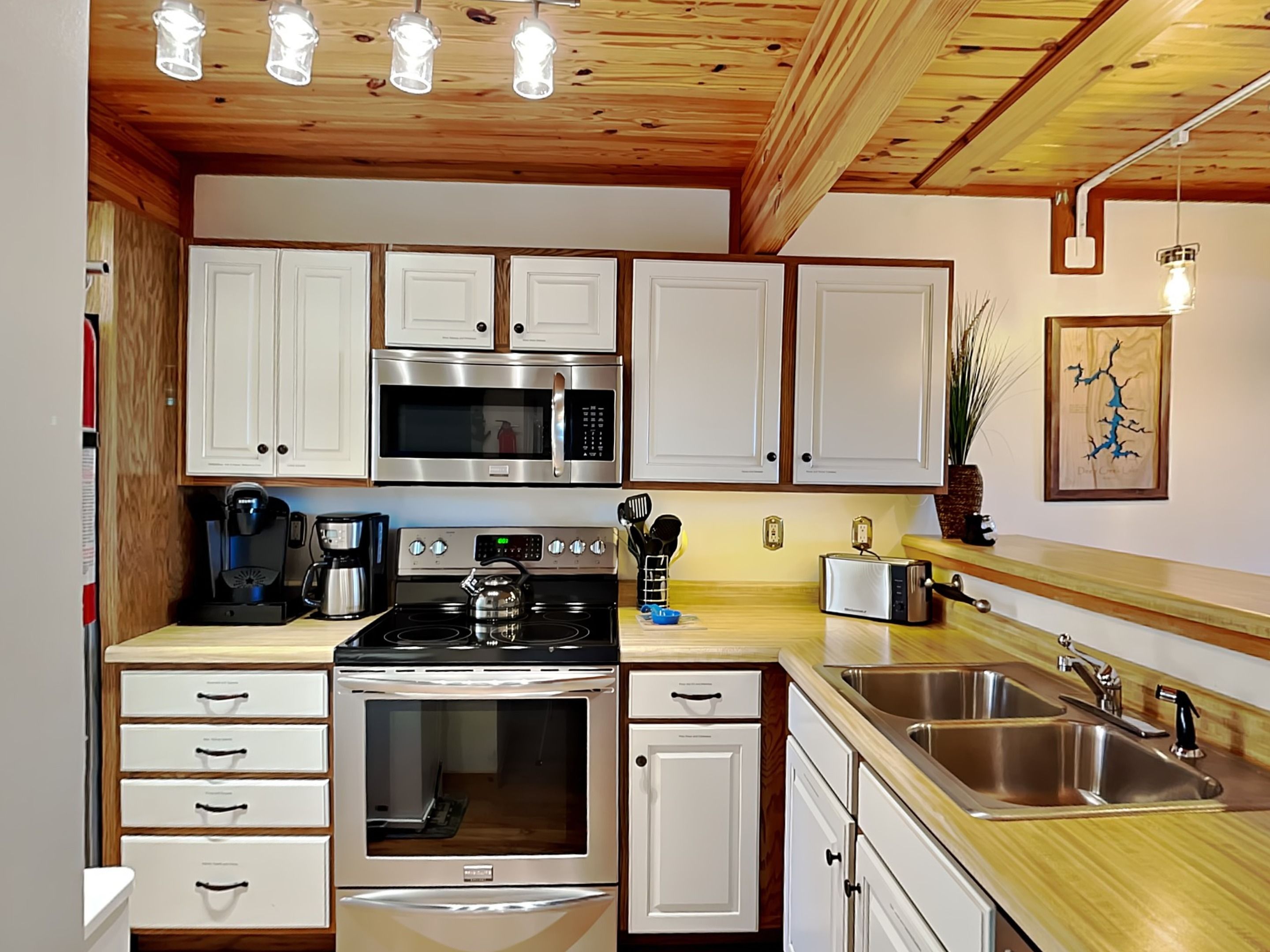 A modern kitchen with white cabinets, stainless steel appliances, a wooden countertop, and a hanging light fixture.