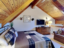 Un dormitorio en el ático con techo de madera, una cama con colcha escocesa, un aparador, un televisor y una guitarra.