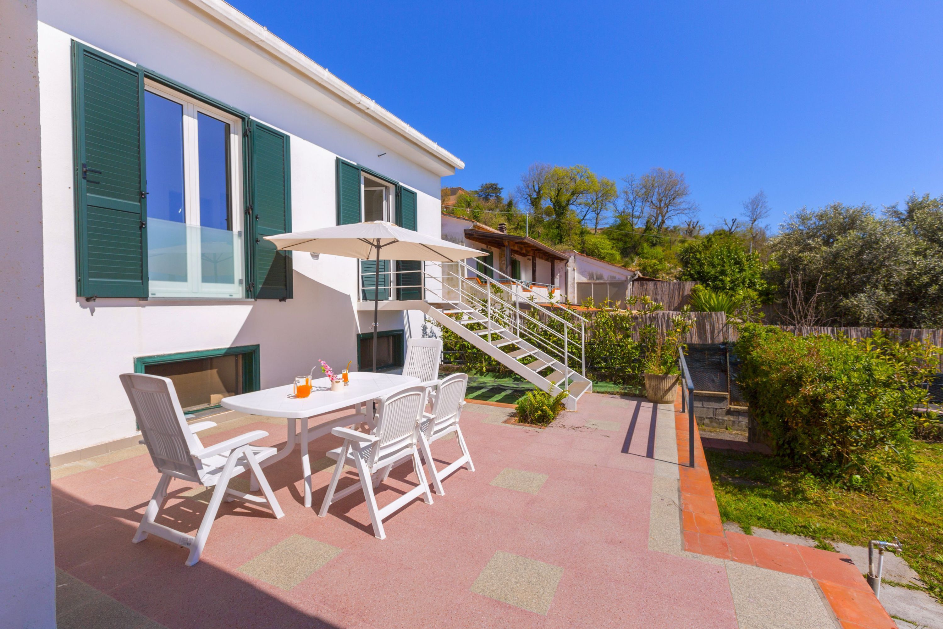 A patio with a table and chairs, a staircase, and a view of the surrounding greenery.