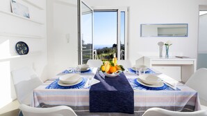 A dining area with a table set for two, a view of the outdoors, and a white interior with a mirror and shelves. - Estate4home - Villa Corinna (Massa Lubrense)