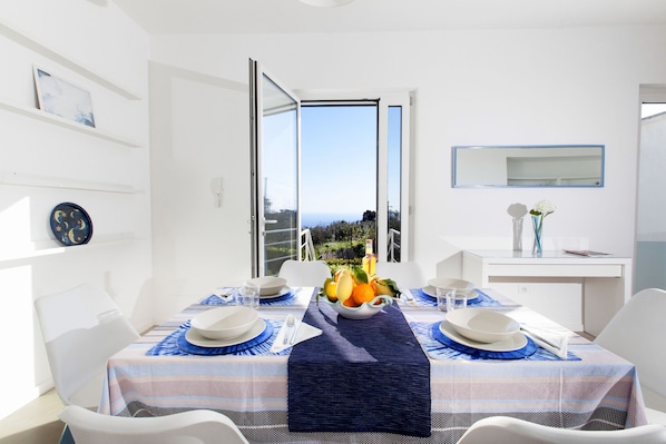 Comedor con una mesa dispuesta para dos personas, vistas al exterior, y un interior blanco con un espejo y estanterías.