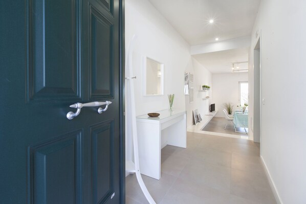 A hallway with a dark wooden door, a white console table with a bowl and vase, and a mirror on the wall. - Estate4home - Villa Corinna (Massa Lubrense)