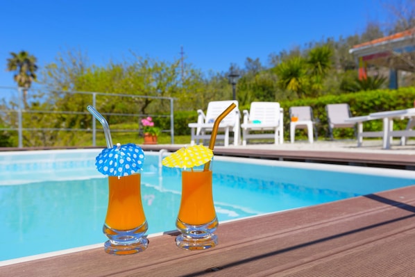 Twee drankjes met parasols op een tafeltje bij het zwembad.