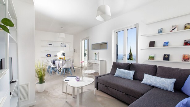 A modern living room with a grey sofa, a white coffee table, and a dining area with a white table and chairs. - Estate4home - Villa Corinna (Massa Lubrense)