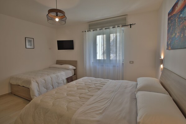 Une chambre avec deux lits, un luminaire au plafond, une fenêtre avec des rideaux et un téléviseur fixé au mur.