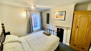 A bedroom with a bed, a window with curtains, a fireplace, and a wooden wardrobe.