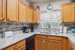A kitchen with wooden cabinets, a granite countertop, a coffee maker, a toaster, and a window with a view.