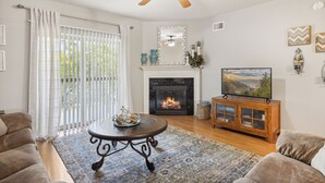 A living room with a fireplace, a ceiling fan, and a television on a wooden cabinet. - 2 Bedroom Condo with River View | Located in Pigeon Forge | Sleeps 6 (Pigeon Forge)