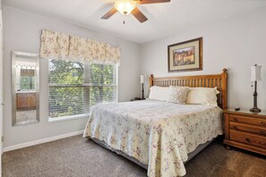 A bedroom with a wooden bed, a nightstand, a lamp, a painting on the wall, and a window with blinds. - 2 Bedroom Condo with River View | Located in Pigeon Forge | Sleeps 6 (Pigeon Forge)