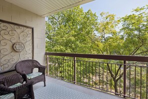 A balcony with a wicker chair and a patterned rug, overlooking a lush green landscape.