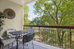 A balcony with a table and chairs, a decorative wall piece, and a view of trees. - Two bedroom, two bathroom with walk in Shower condo located just off the parkway (Pigeon Forge)