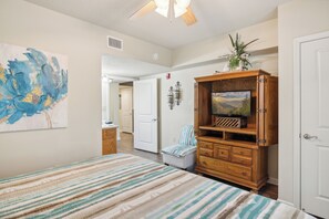 A bedroom with a bed, a wooden cabinet with a television, a door, and a hallway leading to another room. - Two bedroom, two bathroom with walk in Shower condo located just off the parkway (Pigeon Forge)