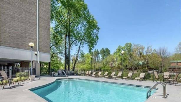A rectangular outdoor swimming pool with a clear blue water, surrounded by lounge chairs and a paved deck.