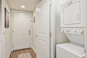 A laundry room with a front-loading washer and dryer, a white door with a picture frame, and a wooden floor.