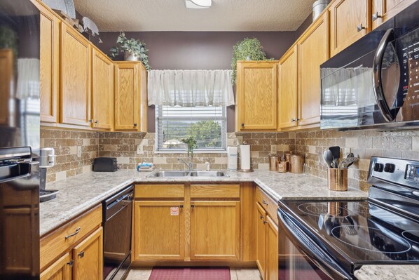 A kitchen with wooden cabinets, a stainless steel refrigerator, a microwave, a stove, and a sink.