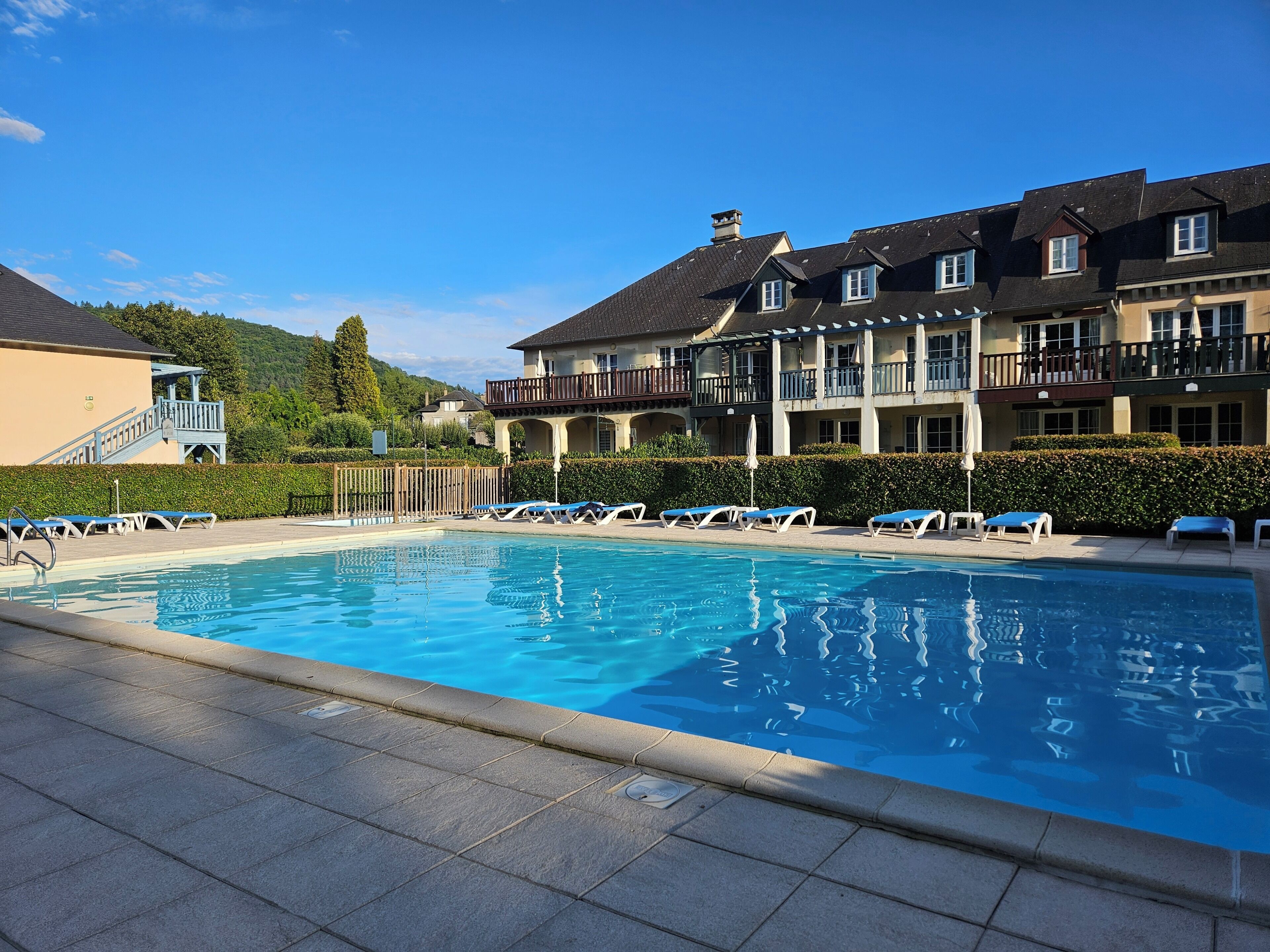 A swimming pool with lounge chairs, a covered deck, and a building with balconies.