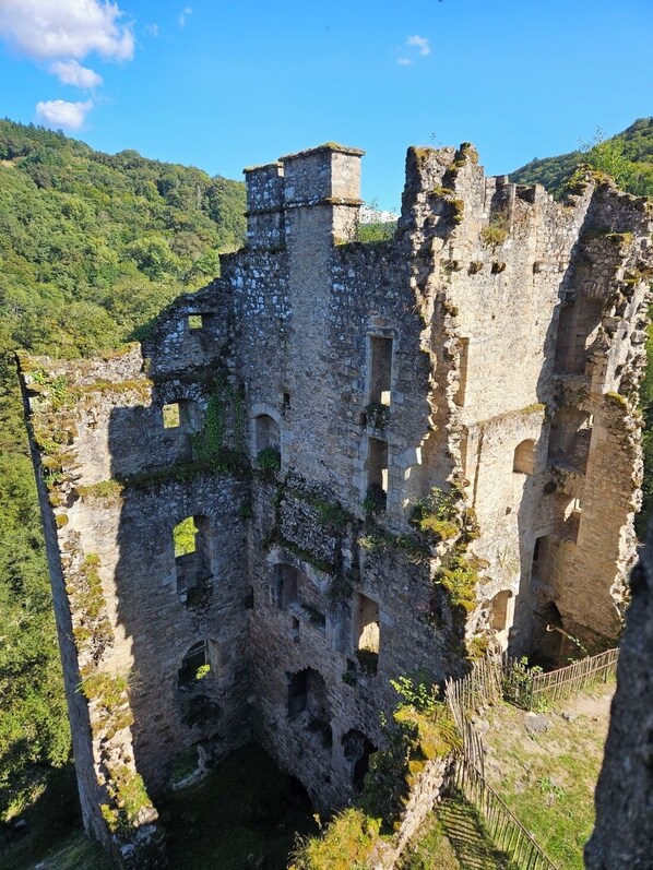 An ancient stone structure with multiple arches and a central tower, surrounded by lush greenery and hills.