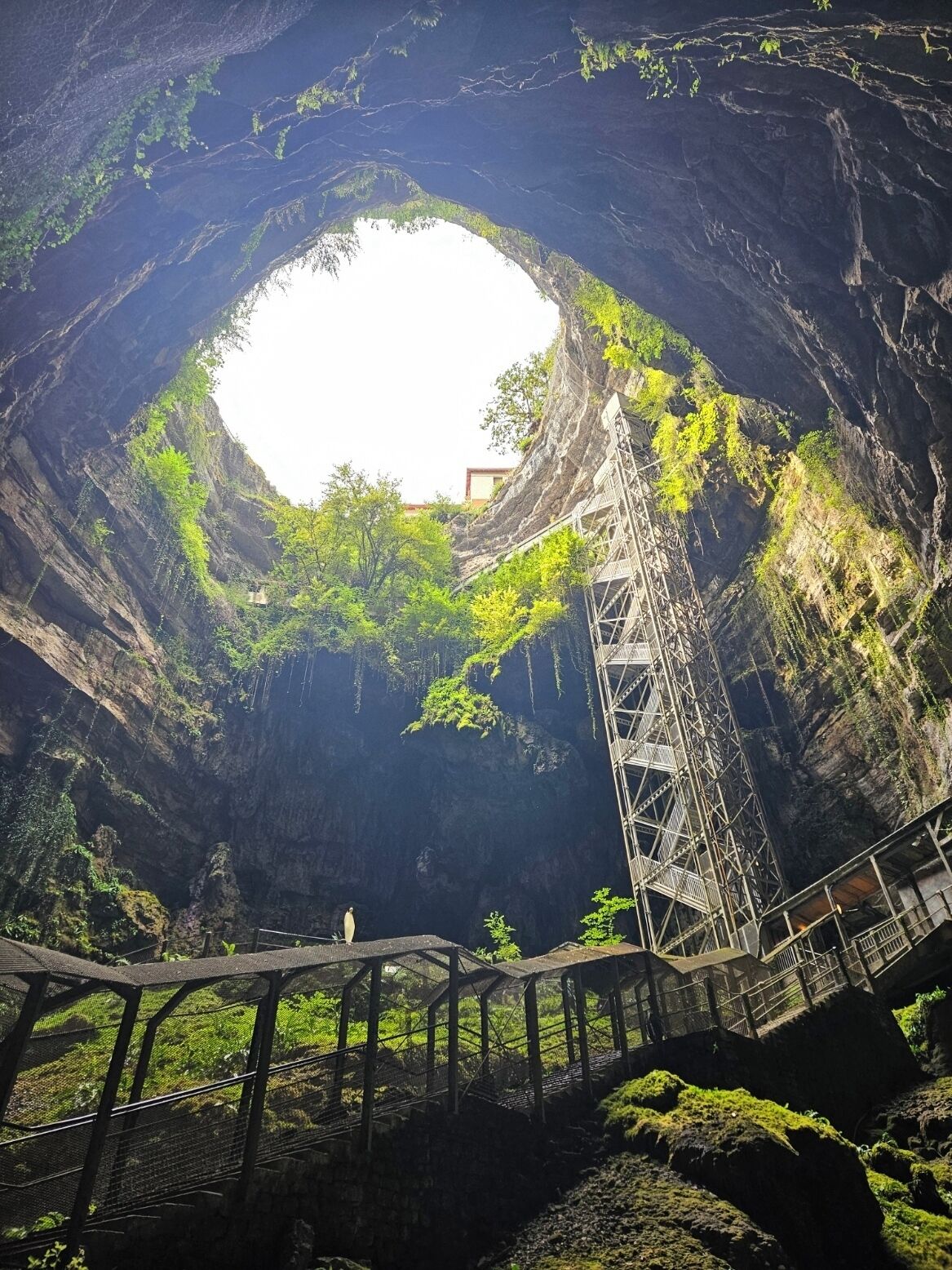 Una gran abertura de cueva con una pasarela metálica y escaleras que conducen al interior.