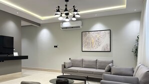A modern living room with a flat-screen TV, a grey sofa, a coffee table, and a contemporary chandelier.