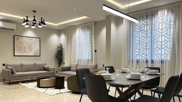 A modern dining area with a round table set for six, surrounded by dark chairs.