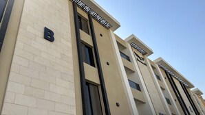 A modern building with a beige facade, large windows, and a prominent 'B' sign.