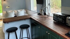 A compact kitchen with a wooden countertop, a built-in oven, and a window with curtains. - Remote hut set in the beautiful Kent Downs (Sittingbourne)