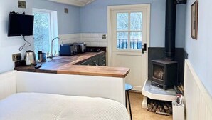 A cozy room with a bed, a kitchen area with a stove, and a TV mounted on the wall. - Remote hut set in the beautiful Kent Downs (Sittingbourne)