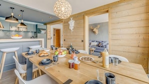 A modern kitchen with a wooden dining table set for breakfast, a fruit bowl, and various breakfast items.