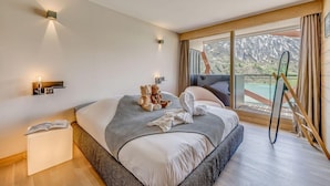 A modern bedroom with a large bed, a bedside table with a lamp, and a view of mountains through the window.