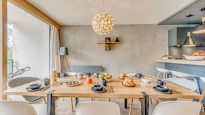 A modern dining area with a wooden table set for breakfast, a hanging light fixture, and a kitchen counter visible in the background.