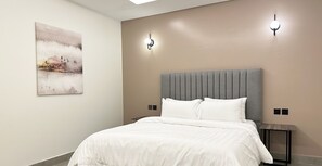 A modern bedroom with a large bed, two wall-mounted lights, and a painting on the wall. - Kease Malqa 31-10 Luxury Gold  AG23 (Riyadh)