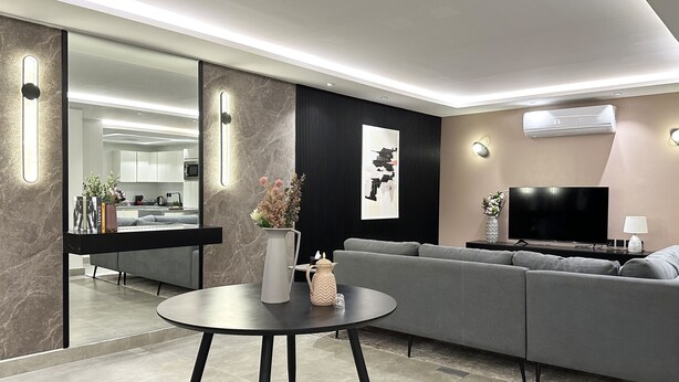 A modern living room with a grey sofa, a round coffee table, and a flat-screen TV. - Kease Malqa 31-10 Luxury Gold  AG23 (Riyadh)