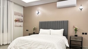 A modern bedroom with a large bed, two bedside tables with lamps, an air conditioning unit, and a wall-mounted light fixture. - Kease Malqa 31-10 Luxury Gold  AG23 (Riyadh)