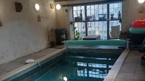 Una piscina interior con vista despejada al techo, un ventanal que ofrece vistas al exterior y una zona de estar con un tapete verde.