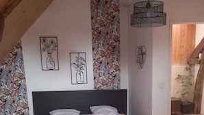 Un dormitorio con cama, cabecera de madera, cortina estampada y lámpara colgante.