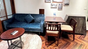A room with a blue sofa, a round wooden table, and a wooden chair. There are framed pictures on the wall. - Fusion Links Apartment (Hanoi)